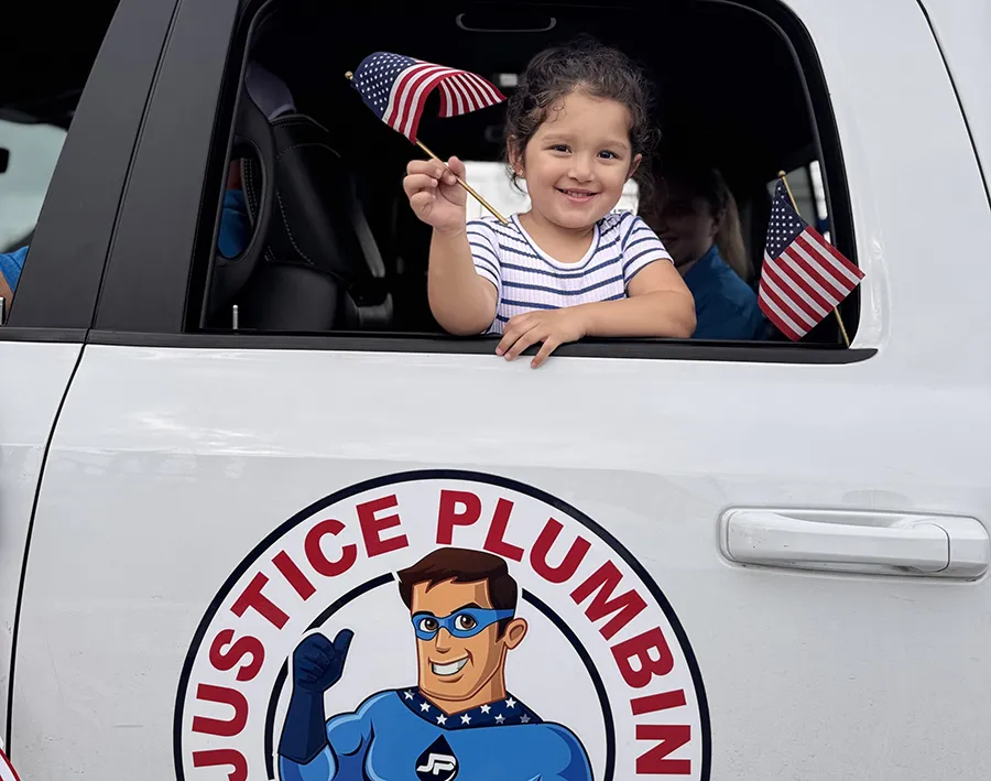 Child waving American flag from Justice Plumbing vehicle in Granbury area parade, showcasing family-friendly local plumbing company and community pride.