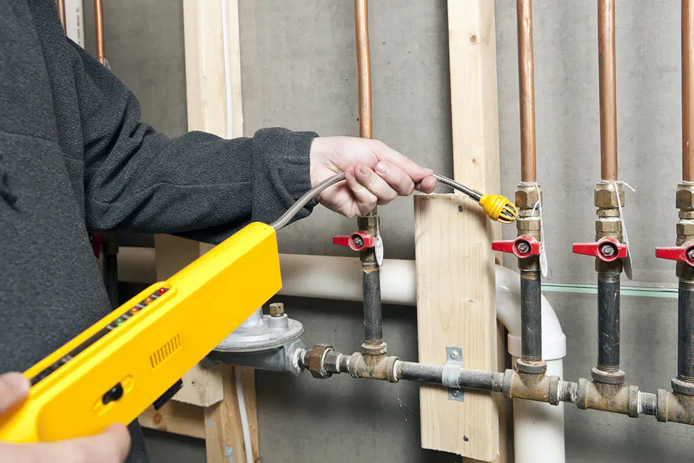 Justice Plumber using a leak detector near a set of house gas lines